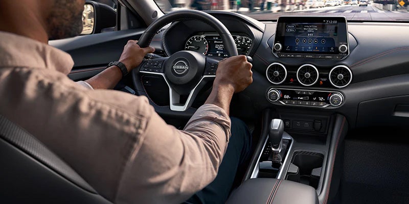 A man with his hands on the wheels, driving a 2024 Nissan Sentra.